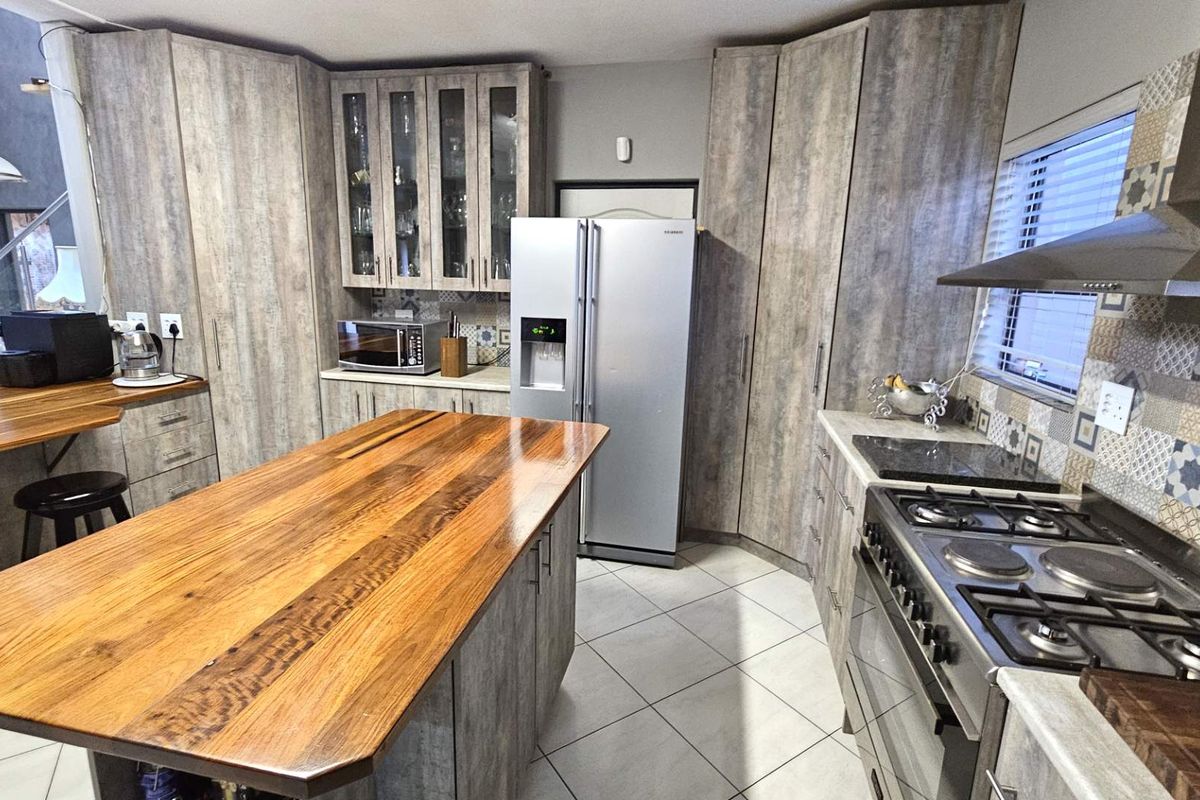 Modern kitchen featuring wood-look cabinetry, a large central island with a timber countertop, stainless steel gas hob, extractor fan, and tiled backsplash.