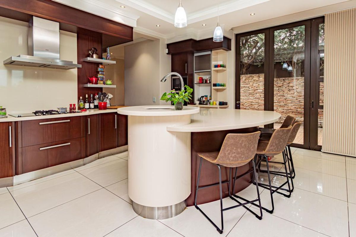 Modern kitchen featuring dark wood cabinetry, stone countertops, a central island with integrated sink, and direct access to the outdoor patio area.