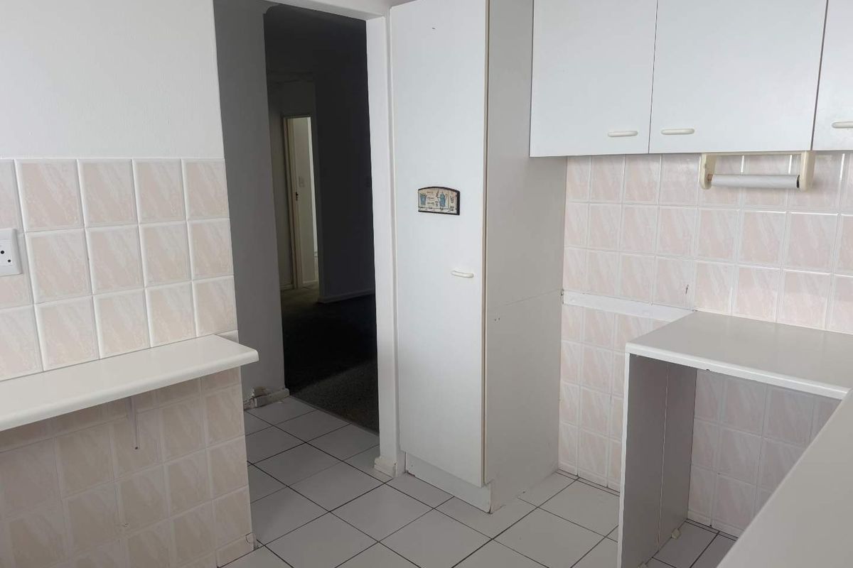 A functional kitchen area featuring tiled splashbacks, built-in cabinetry, and tiled flooring, providing a basic layout ready for potential modernization.