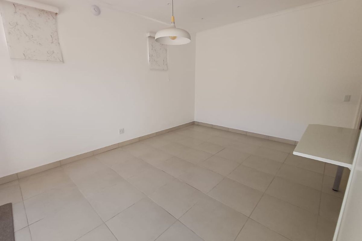 A bright, empty living area featuring neutral tiled flooring, a modern pendant light, and a built-in counter, offering a clean canvas for personalization.
