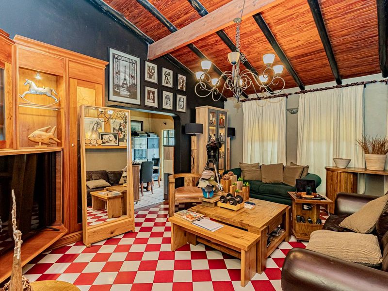 A living room featuring exposed timber ceiling beams, built-in wooden cabinetry, and distinctive red and white checkered floor tiles with an arched transition to adjacent space.
