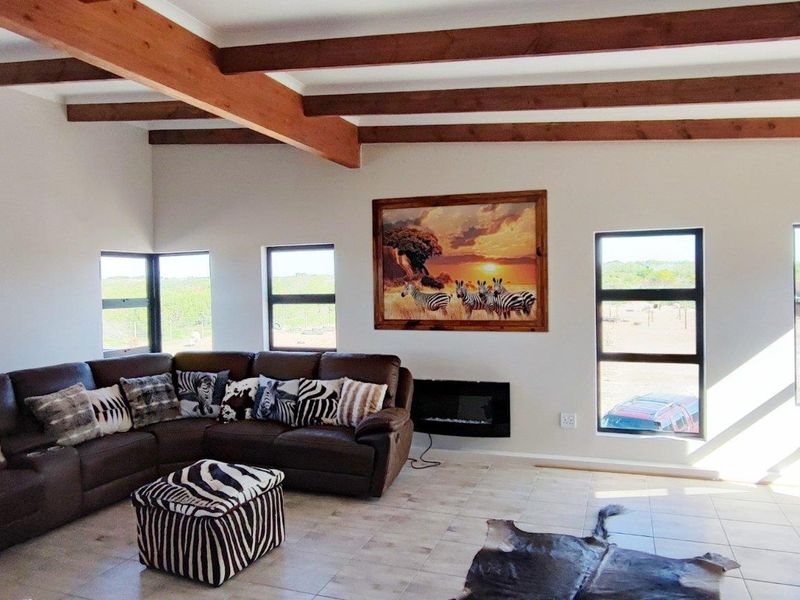 Spacious living room featuring exposed timber ceiling beams, tiled flooring, and a wall-mounted electric fireplace with large windows offering scenic farm views.