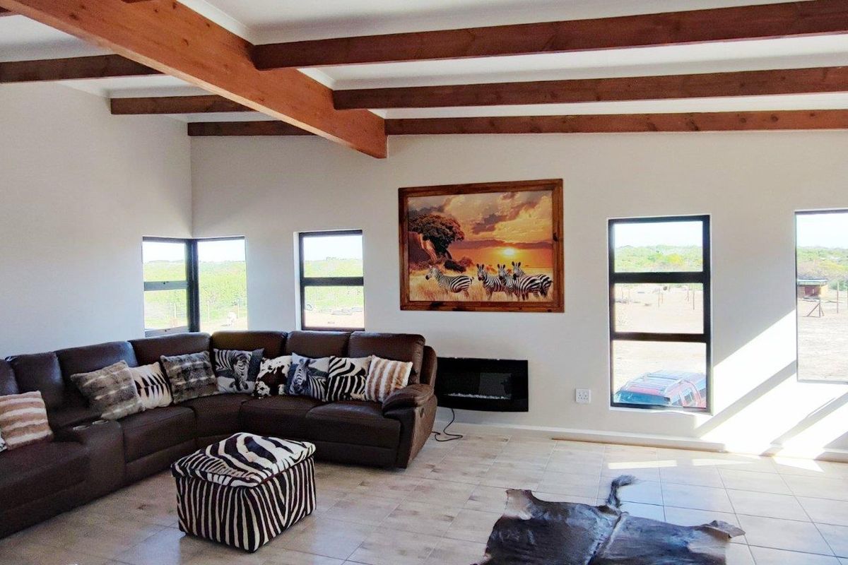 Spacious living room featuring exposed timber ceiling beams, tiled flooring, and a wall-mounted electric fireplace with large windows offering scenic farm views.