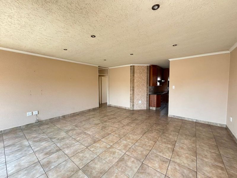 Spacious open-plan living area featuring tiled flooring, recessed lighting, and a tiled feature pillar, leading into a compact kitchen space.