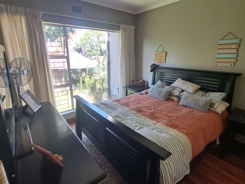 A well-lit bedroom featuring laminate flooring and a large window providing natural light and garden views.