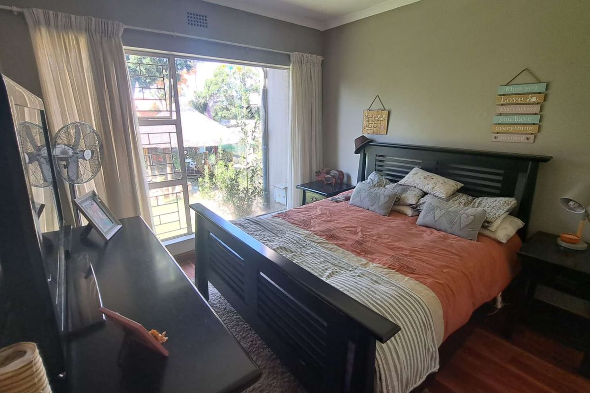A well-lit bedroom featuring laminate flooring and a large window providing natural light and garden views.