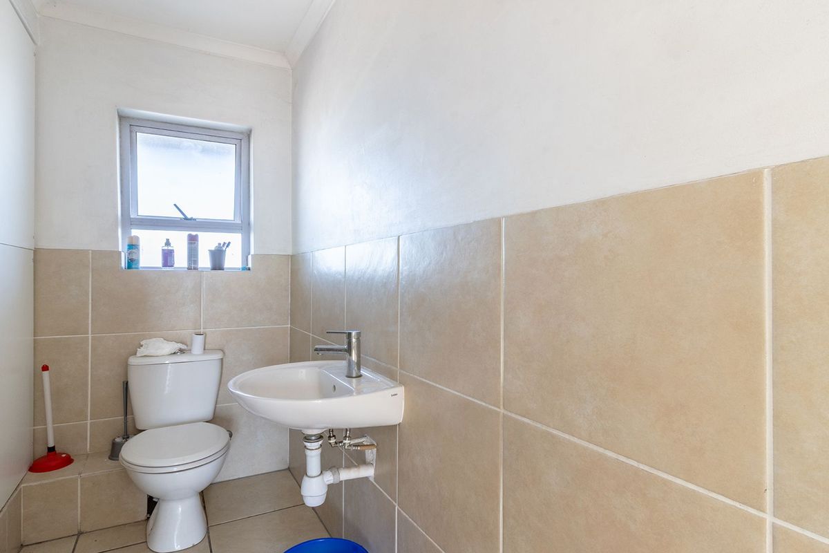 A functional bathroom featuring a wall-mounted basin, standard toilet, and neutral ceramic wall and floor tiling.