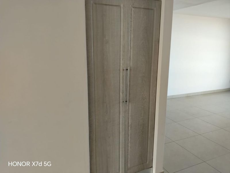 A clean, neutral hallway featuring a modern built-in cupboard with wood-grain finish and light-colored floor tiles.