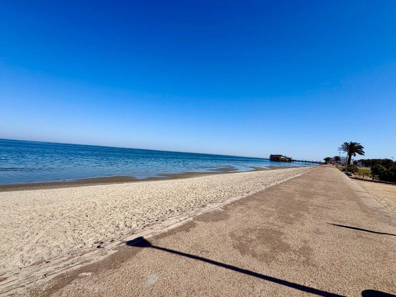 A scenic view of the coastline featuring a sandy beach and a paved walkway along the waterfront.