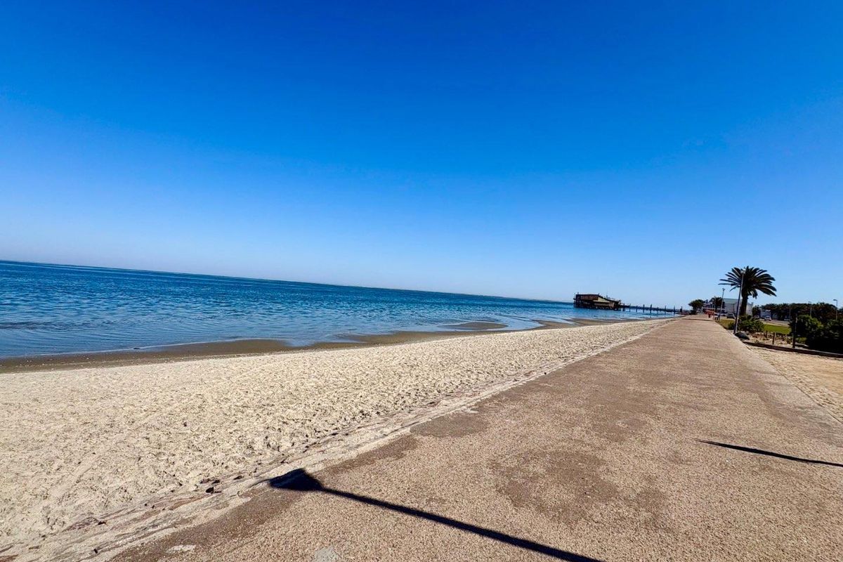 A scenic view of the coastline featuring a sandy beach and a paved walkway along the waterfront.
