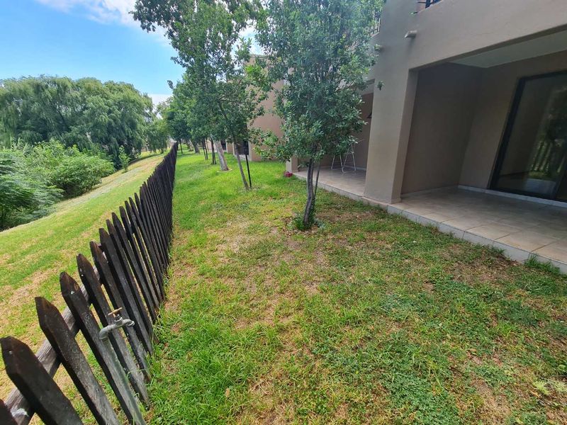 A rear view of the apartment featuring a tiled patio, a private garden area, and a wooden picket fence boundary.