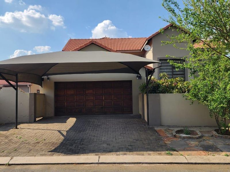 Front exterior view of the townhouse featuring a paved driveway, a shade sail carport, and a wooden garage door.