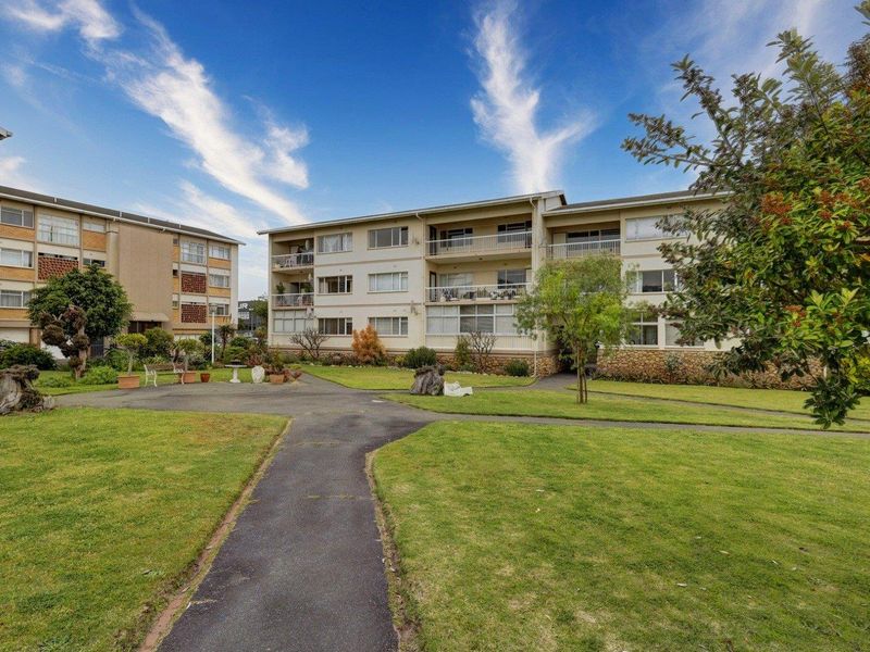 Exterior view of the apartment complex featuring landscaped gardens, paved walkways, and private balconies on the building facade.
