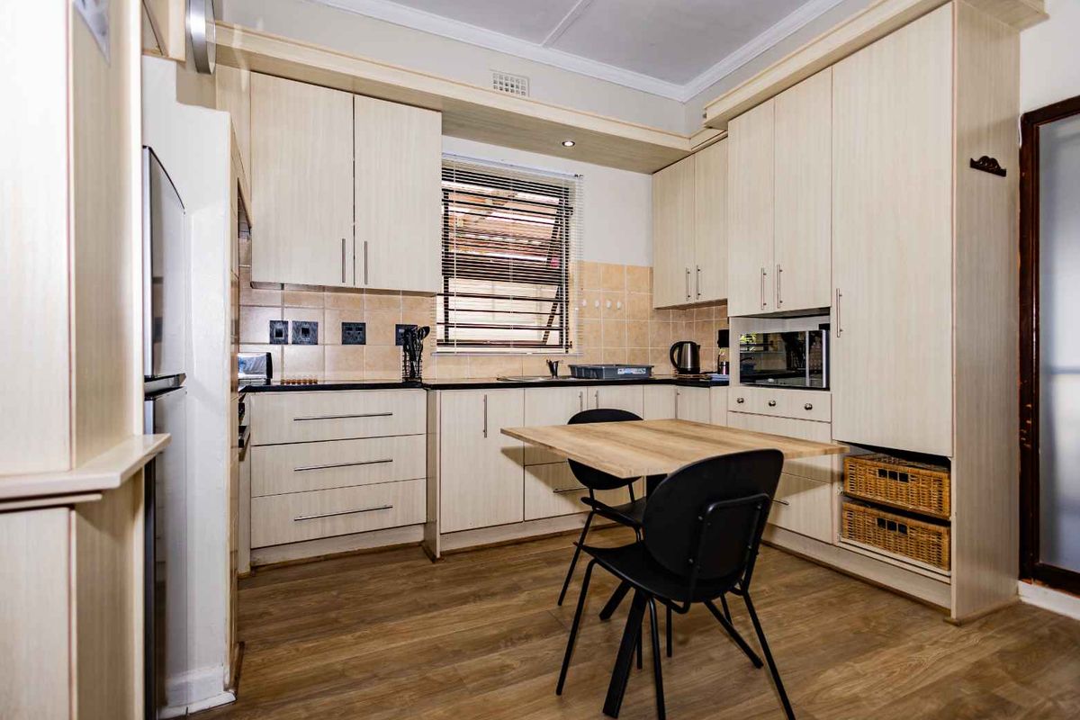 A functional kitchen featuring light wood-grain cabinetry, laminate countertops, a built-in microwave, and a tiled splashback with integrated sink and hob area.