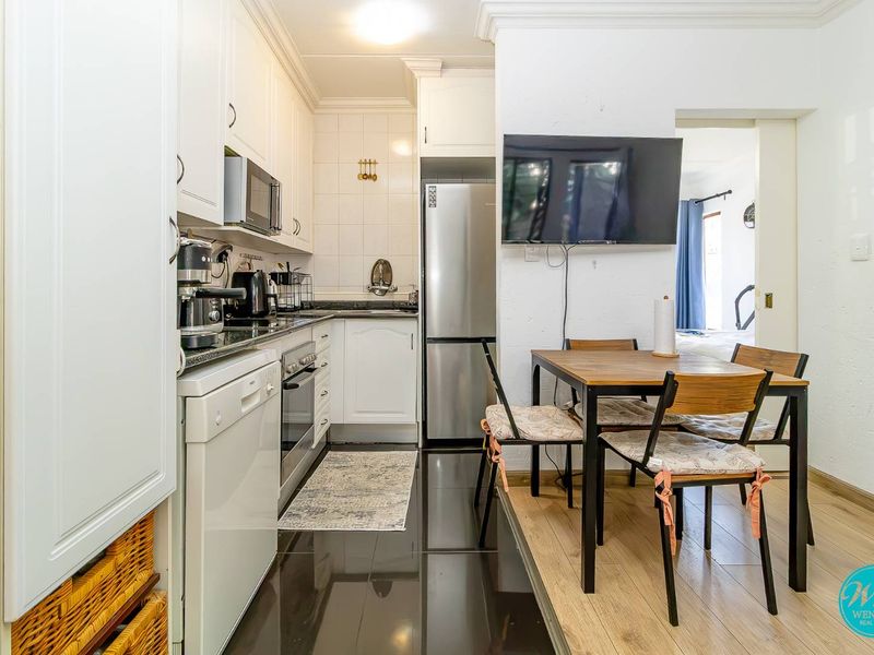 Compact open-plan kitchen and dining area featuring white cabinetry, granite countertops, built-in appliances, and a mix of tiled and laminate flooring.
