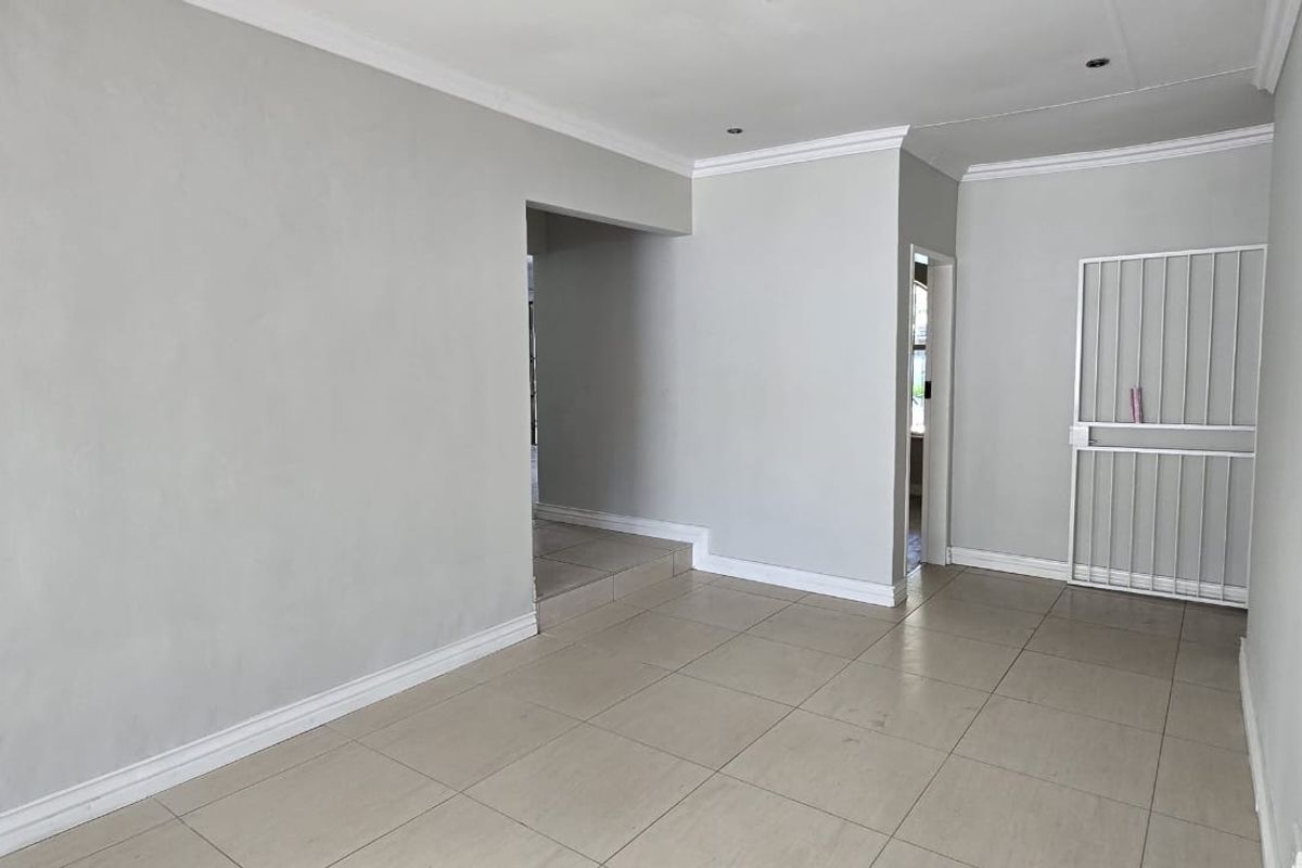 A bright, empty living area featuring neutral tiled flooring, crown molding, and a secure metal gate leading to an adjacent space.