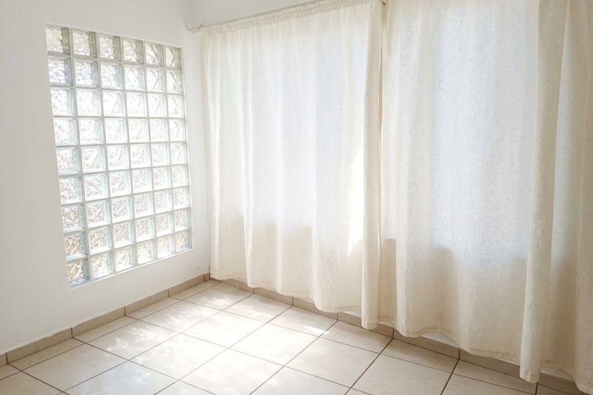 A bright, empty living area featuring ceramic floor tiles and a distinctive glass block feature wall, providing ample natural light.