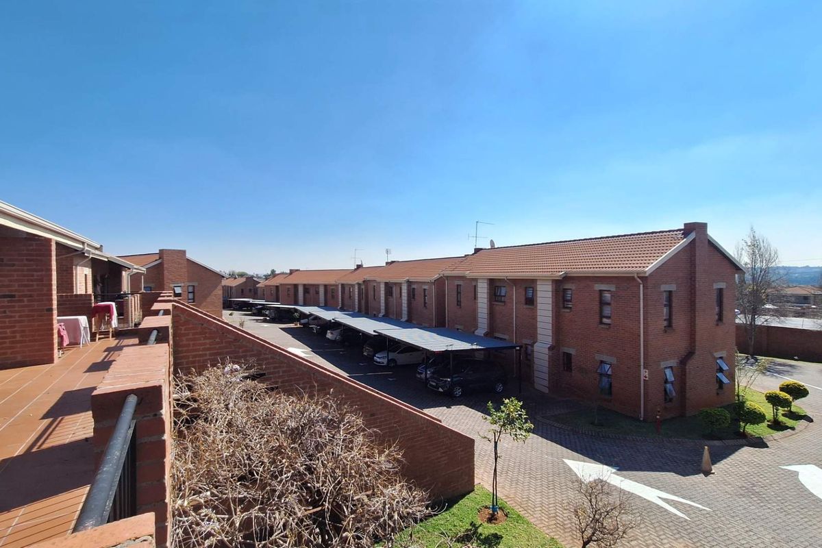 An elevated view of a residential apartment complex featuring brick buildings, tiled roofs, paved driveways, and covered parking bays.