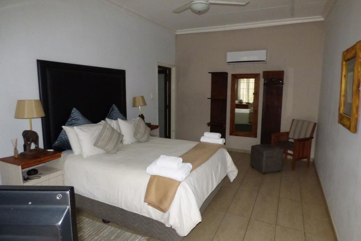 A spacious bedroom featuring tiled flooring, a wall-mounted air conditioning unit, and a ceiling fan, providing a comfortable and functional guest accommodation space.
