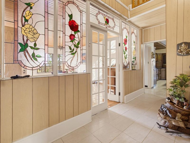 A bright hallway featuring decorative stained glass partitions, timber wall paneling, and tiled flooring, providing a unique transition between living spaces.