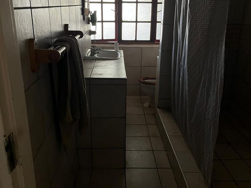 A dated bathroom featuring a built-in vanity, basin, toilet, and shower area with tiled finishes and natural light from a window.