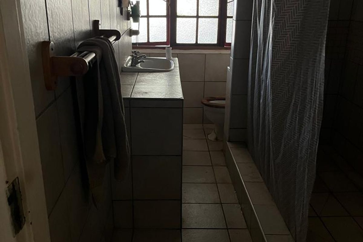A dated bathroom featuring a built-in vanity, basin, toilet, and shower area with tiled finishes and natural light from a window.