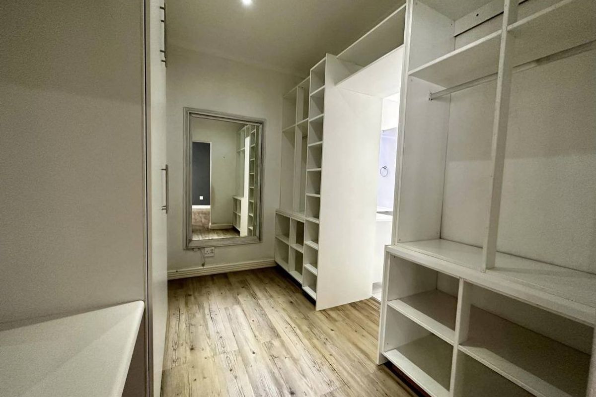 A well-maintained walk-in dressing room featuring extensive built-in white cabinetry, shelving, and wood-look flooring.