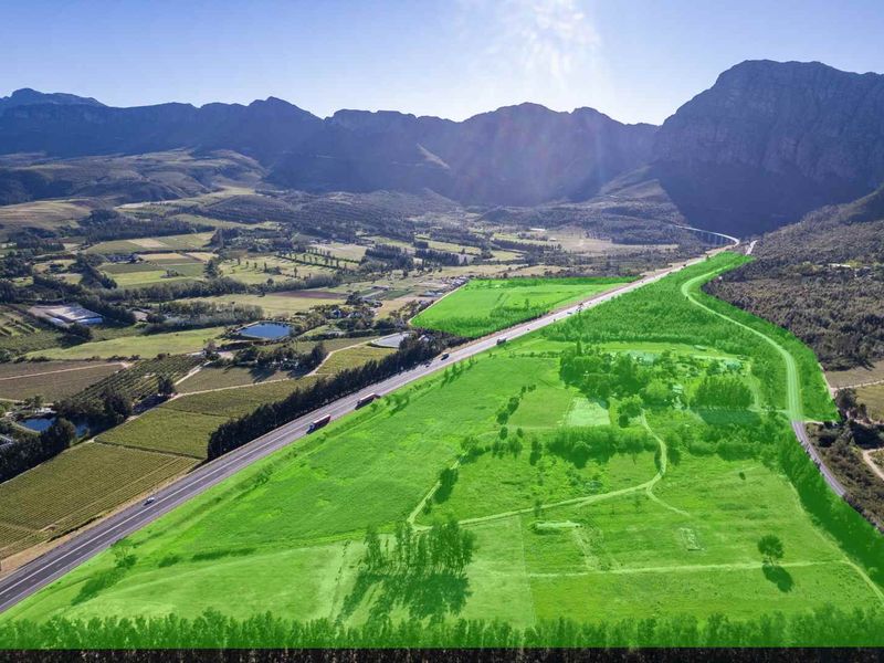Aerial view of a large farm property featuring expansive green pastures, mountain backdrop, and convenient access to the main road.