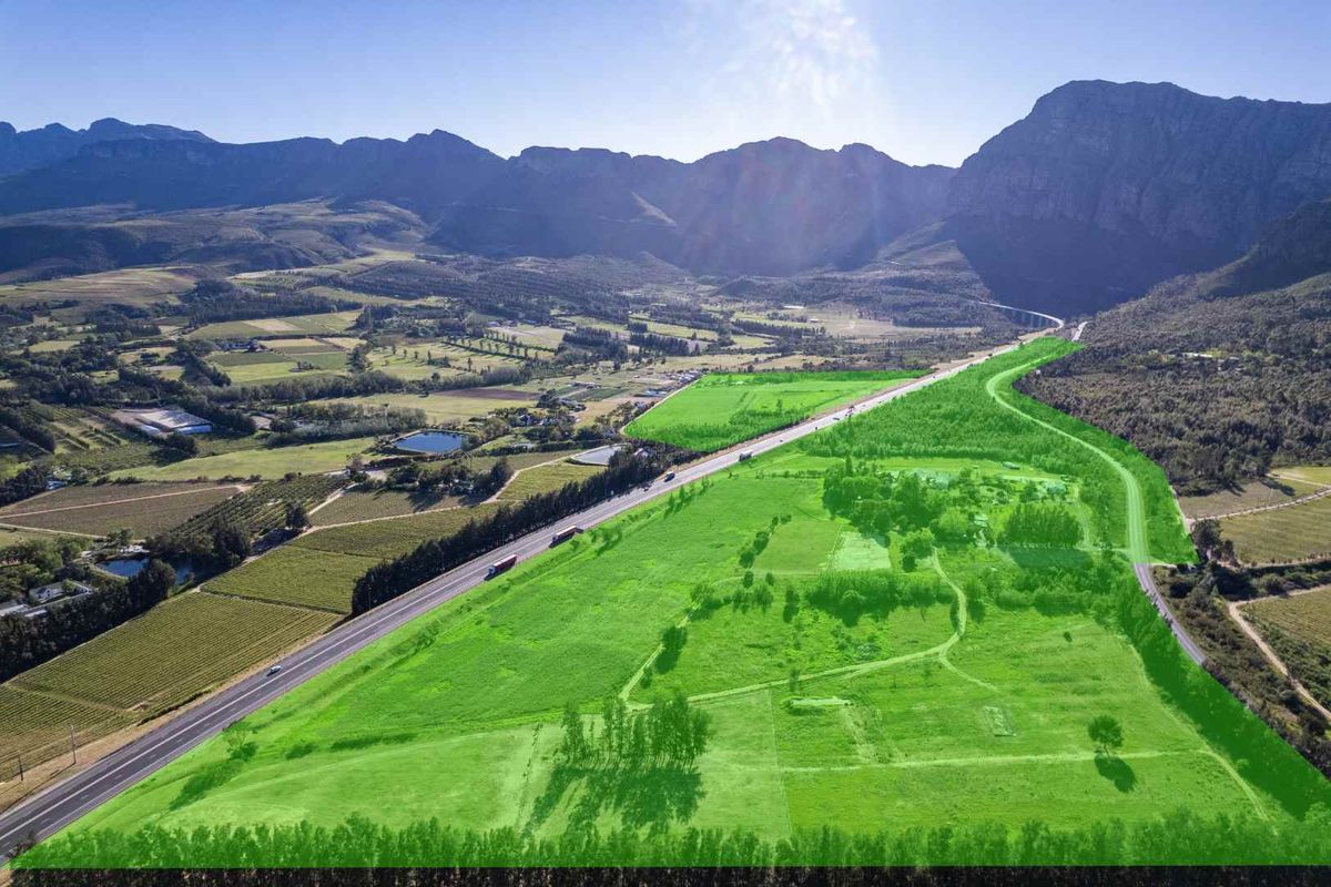 Aerial view of a large farm property featuring expansive green pastures, mountain backdrop, and convenient access to the main road.