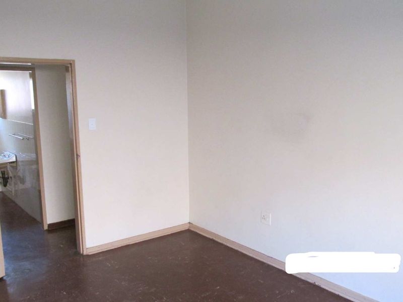 An empty bedroom featuring plain walls and dark flooring, with an adjacent view into a bathroom area.