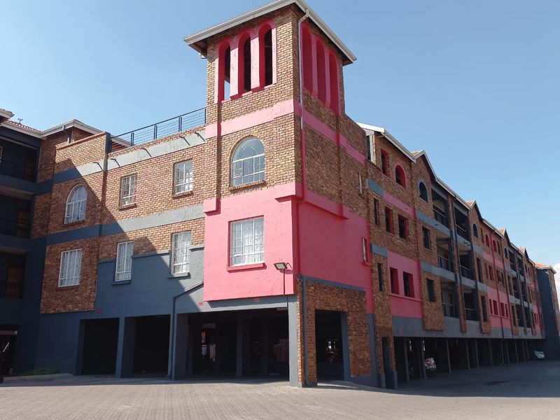 Exterior view of a multi-story apartment complex featuring brick and painted facade, arched windows, and ground-level covered parking bays.