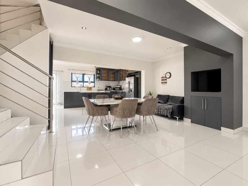 Modern open-plan living and dining area featuring sleek porcelain tiles, a contemporary staircase, and a well-appointed kitchen with dark cabinetry.