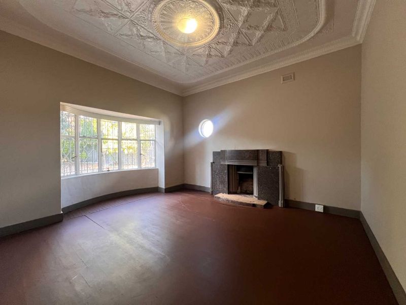 Spacious living room featuring a decorative plaster ceiling, stone fireplace, and a large bay window with security bars.