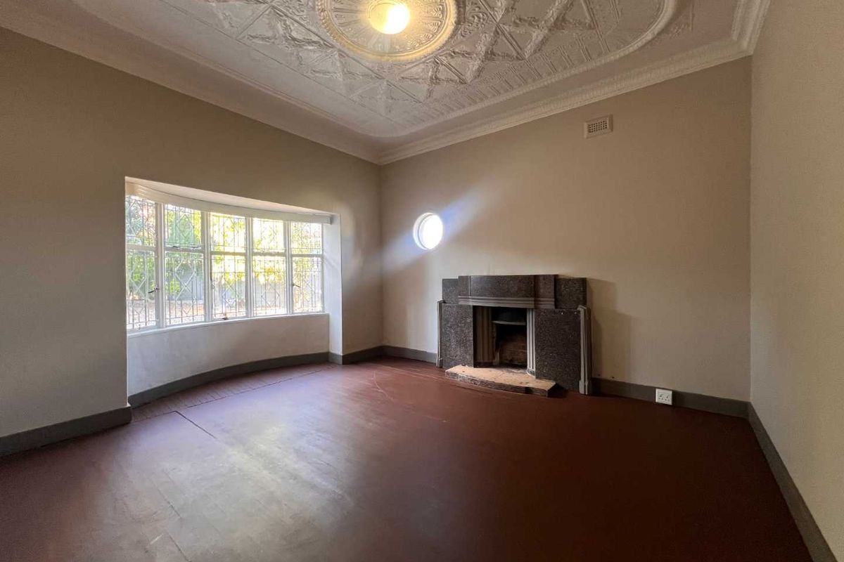 Spacious living room featuring a decorative plaster ceiling, stone fireplace, and a large bay window with security bars.