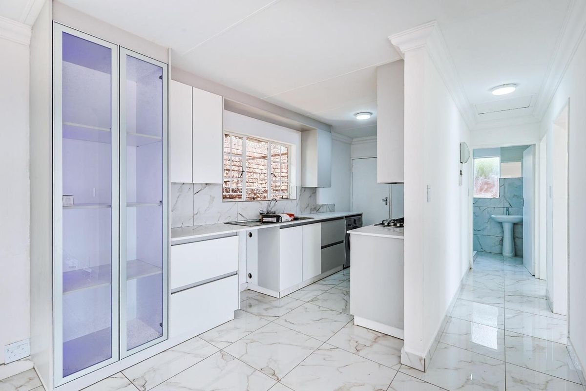 Modern kitchen featuring white cabinetry, marble-look tiled flooring, and integrated storage, leading into a bright hallway with a pedestal basin.