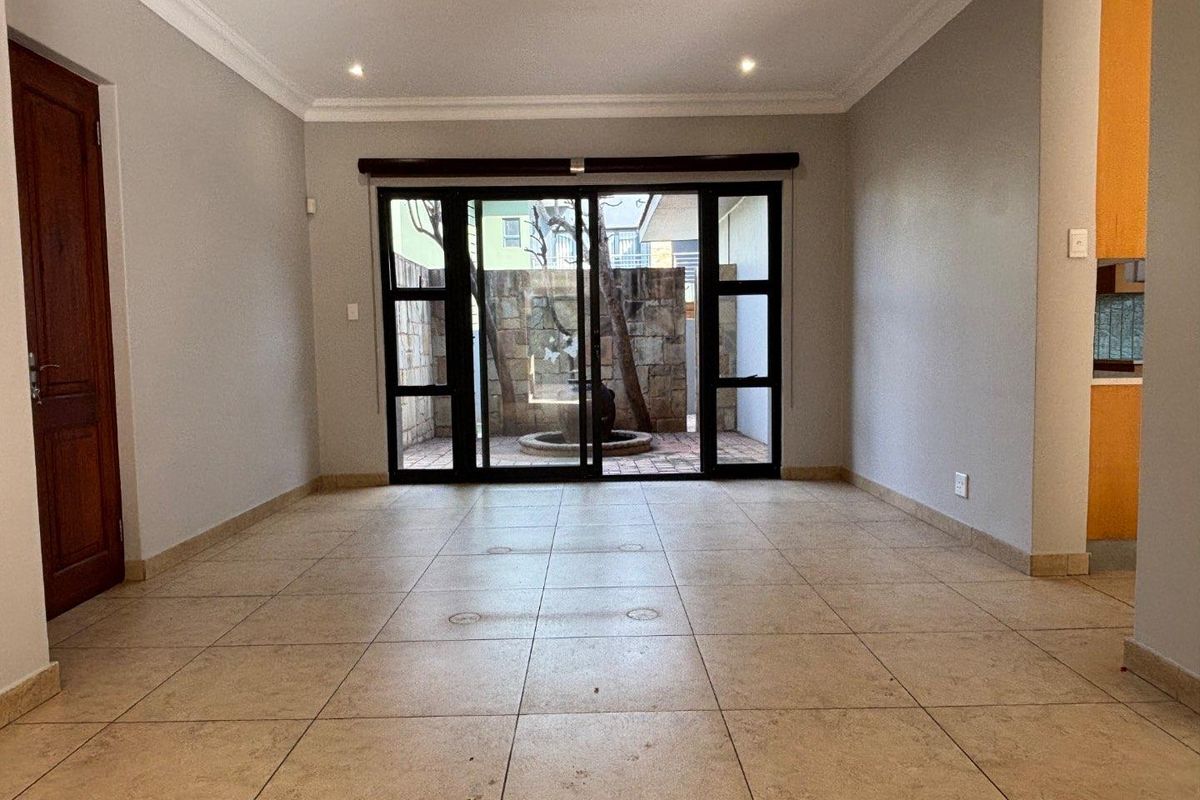 An open-plan living area featuring tiled flooring, recessed ceiling lighting, and large sliding glass doors that open to a private courtyard.