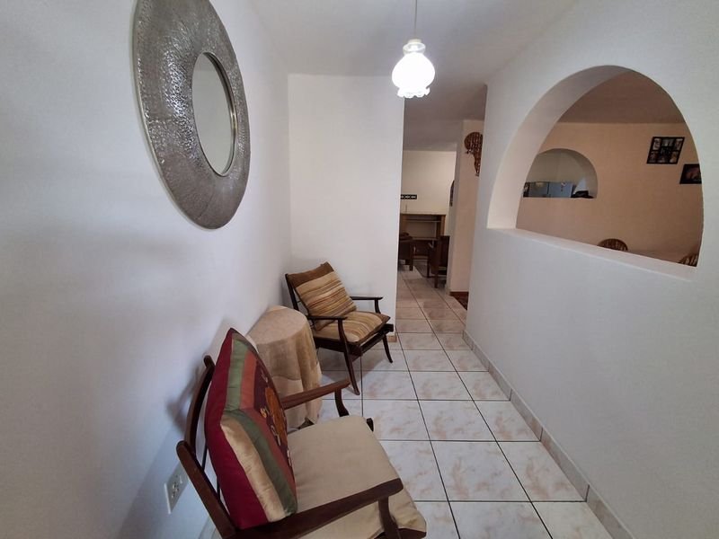 A tiled hallway featuring an arched wall opening that connects to adjacent living spaces, illuminated by a central pendant light fixture.