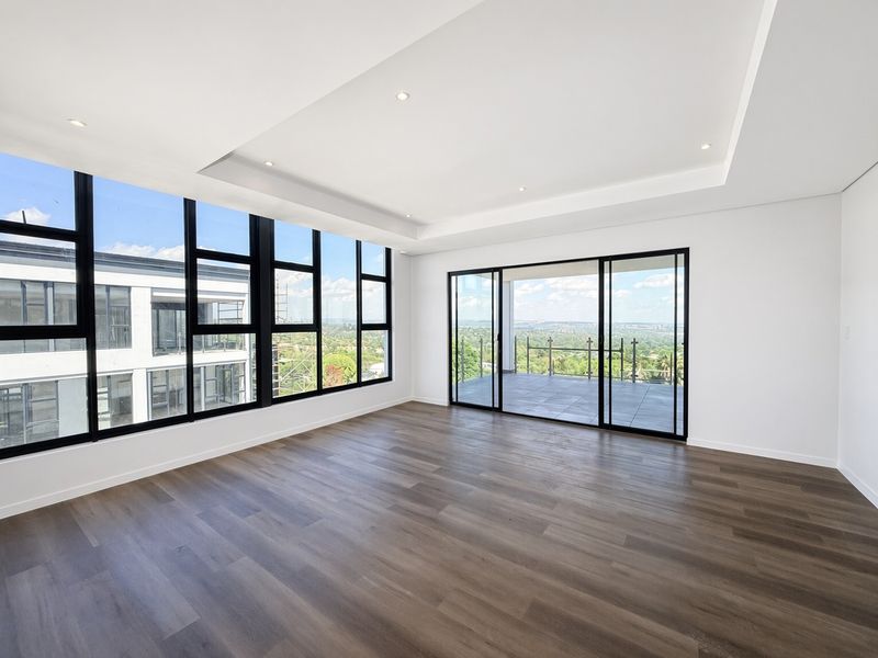 Spacious, modern living area featuring high ceilings with recessed lighting, large windows, and sliding doors leading to a balcony with expansive views.