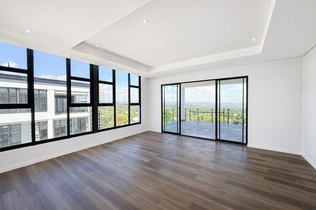 Spacious, modern living area featuring high ceilings with recessed lighting, large windows, and sliding doors leading to a balcony with expansive views.