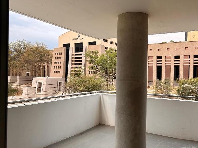 A covered balcony featuring tiled flooring, a structural concrete column, and a metal balustrade, offering an urban view of the nearby Supreme Court building.