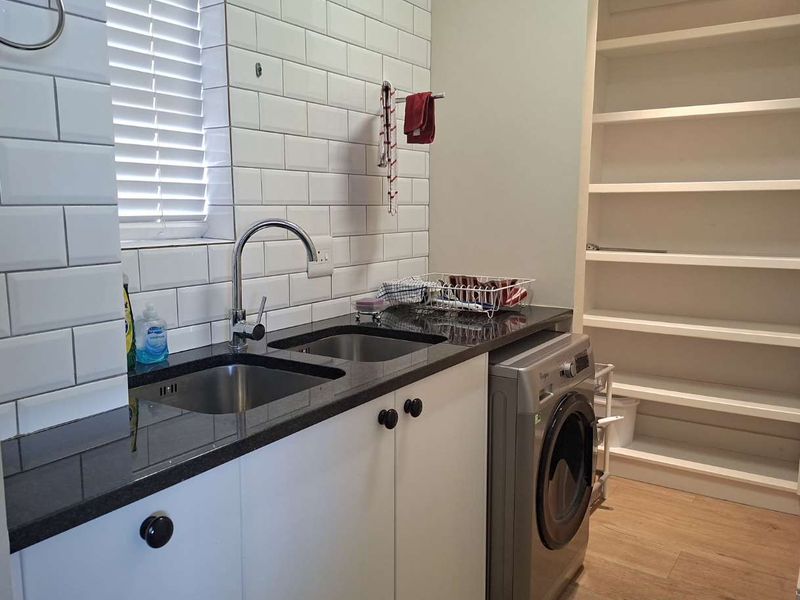 A functional scullery featuring a double stainless steel sink, granite countertops, subway tile backsplash, and ample built-in shelving for storage.