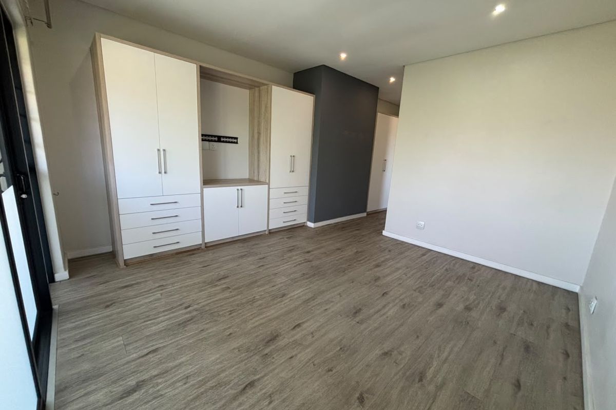 A bright and modern bedroom featuring neutral walls, wood-look laminate flooring, and extensive built-in cabinetry with integrated storage.