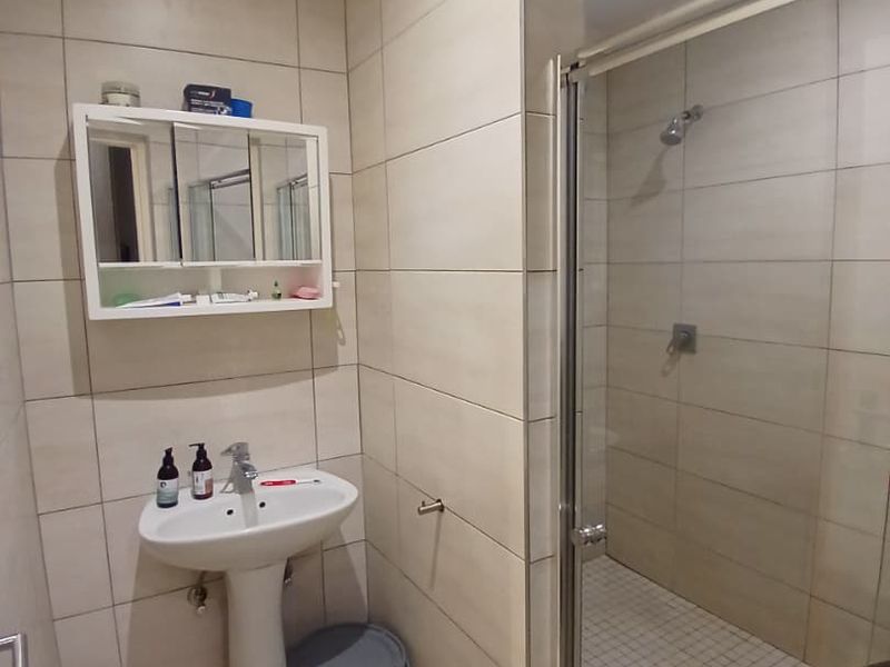 A functional bathroom featuring a pedestal basin, wall-mounted medicine cabinet, and a glass-enclosed shower with neutral wall and floor tiling.