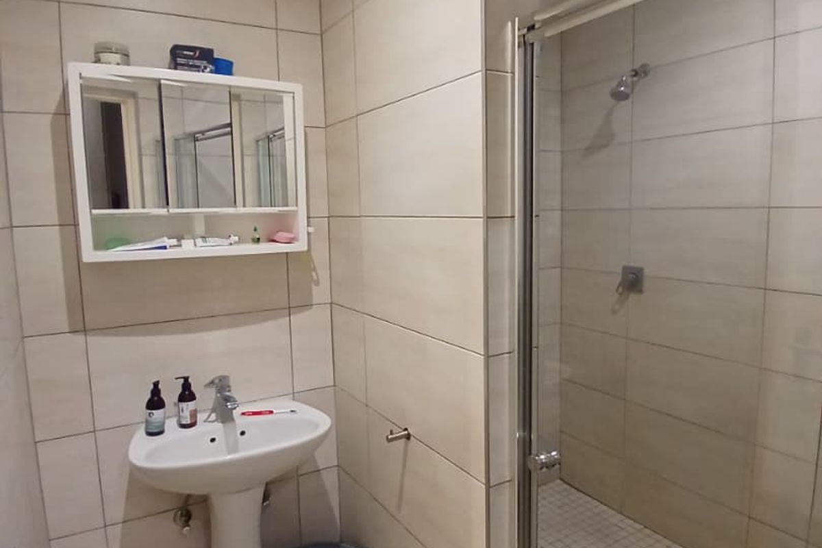 A functional bathroom featuring a pedestal basin, wall-mounted medicine cabinet, and a glass-enclosed shower with neutral wall and floor tiling.