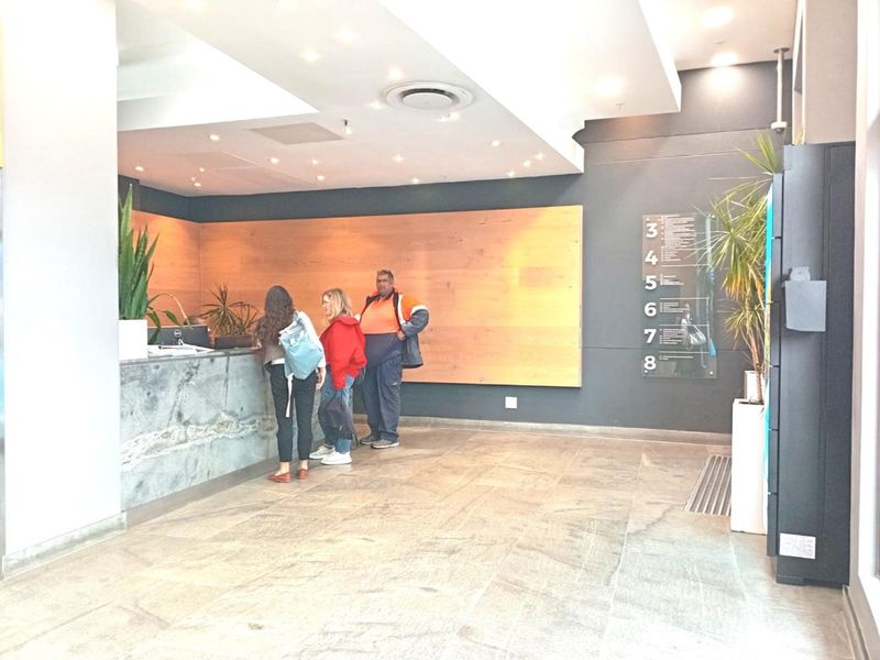 Modern office building lobby featuring a stone reception desk, wood-paneled accent wall, and clear floor directory signage.