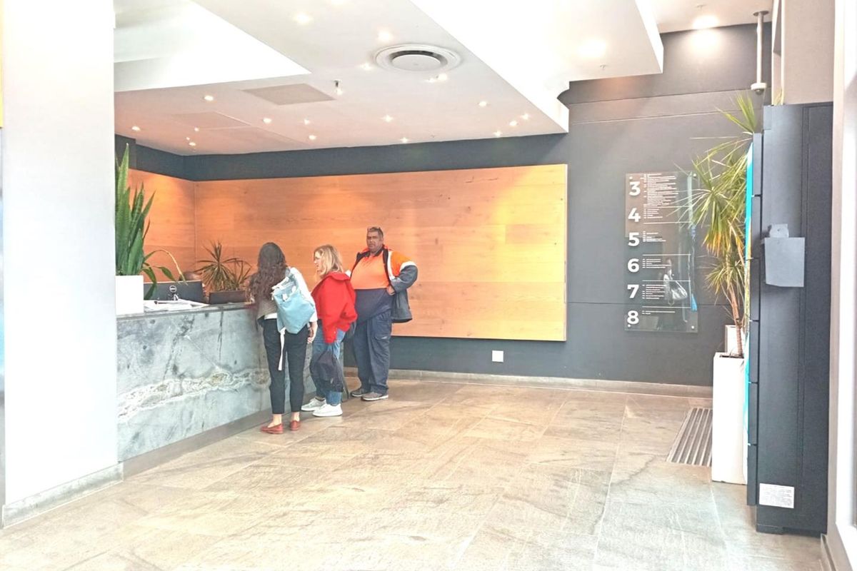 Modern office building lobby featuring a stone reception desk, wood-paneled accent wall, and clear floor directory signage.