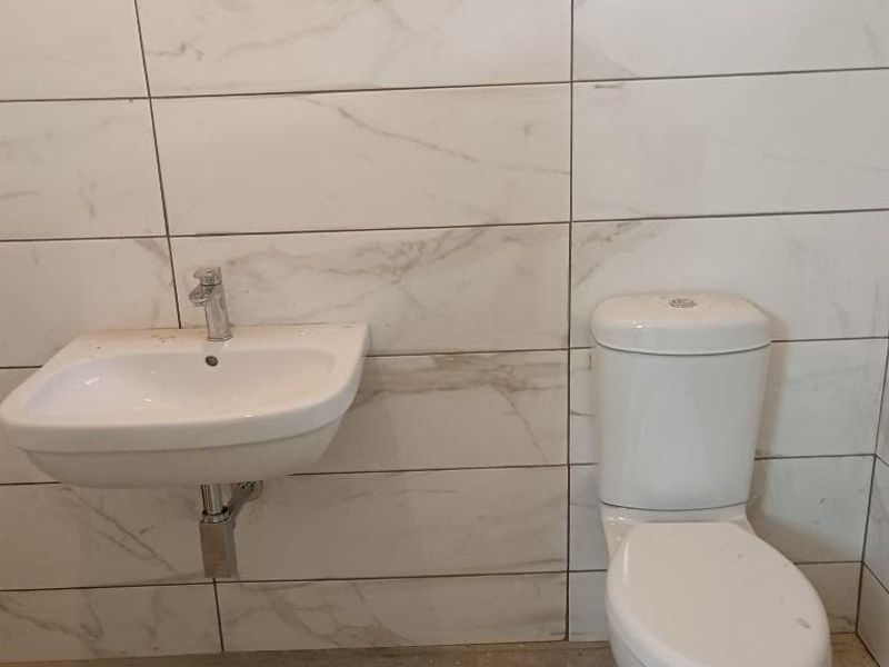 A modern bathroom featuring marble-effect wall tiles, a wall-mounted basin, and a close-coupled toilet, currently awaiting final flooring installation.