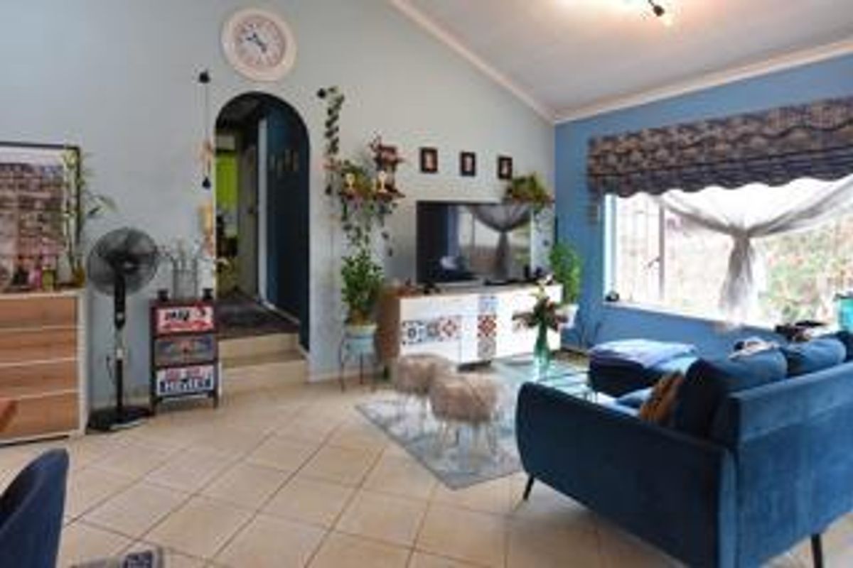 A spacious living room featuring tiled flooring, a vaulted ceiling, and an arched doorway leading to an adjacent area.