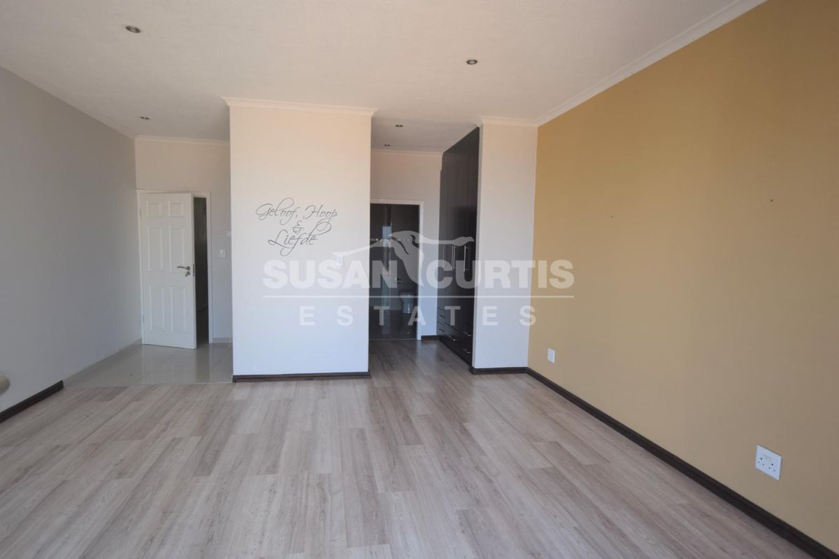 A spacious, empty bedroom featuring light wood-look laminate flooring, recessed ceiling lighting, and built-in dark cabinetry.