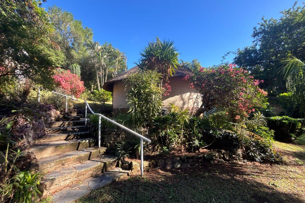 A charming cottage exterior featuring a traditional thatched roof, stone retaining walls, and a stone staircase with a metal handrail set in a garden.